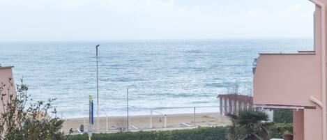 A coastal view with a beach, a fence, and a clear sky.