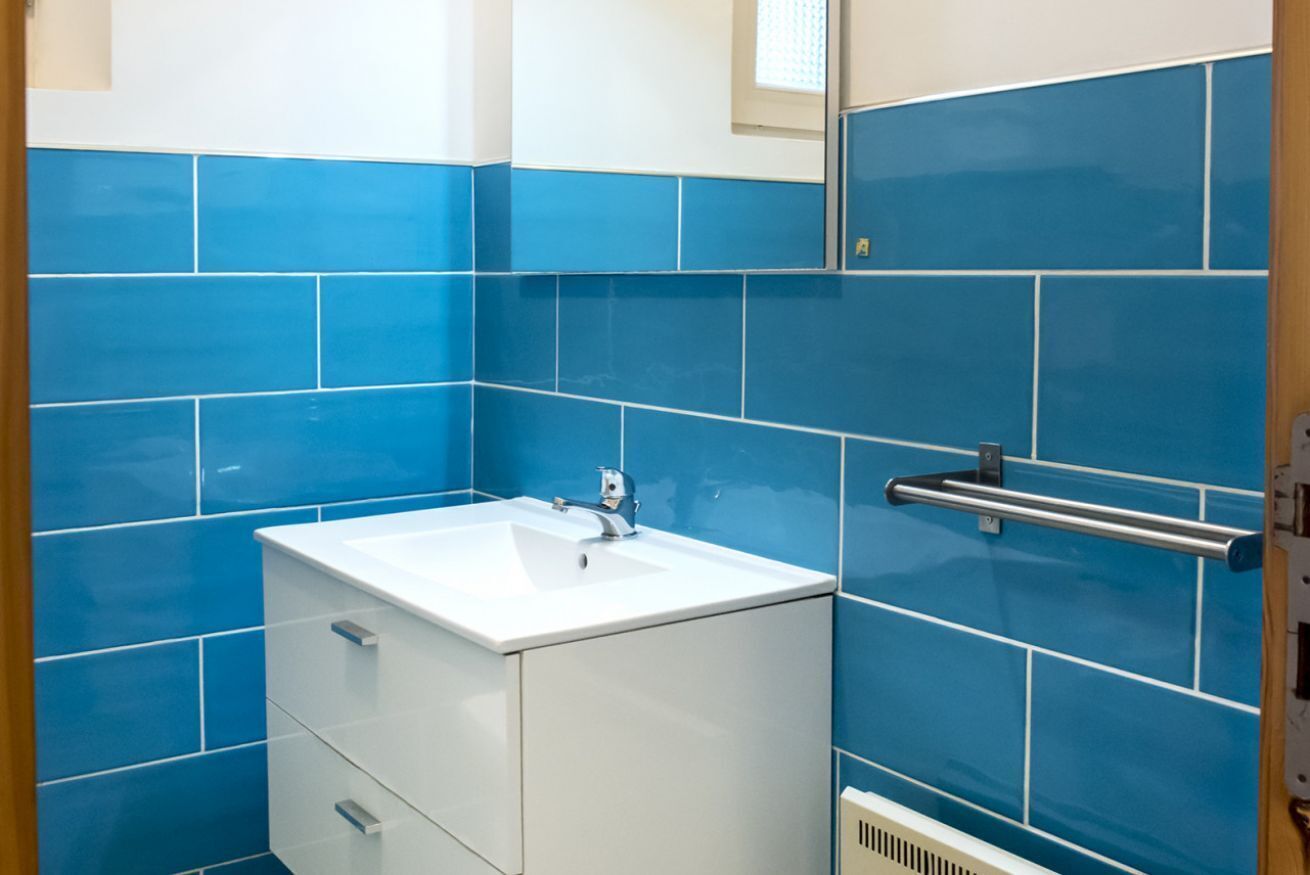 A bathroom with blue tiles, a white sink, and a handrail.