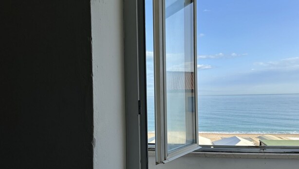 Ett rum med ett stort fönster med utsikt över en strand.