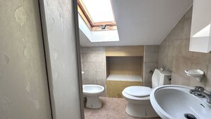 Ett badrum med två toaletter, ett handfat och ett takfönster.