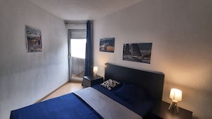 Ein Schlafzimmer mit einem Bett, zwei Nachttischen, einem Fenster mit Vorhängen und Wandbildern.