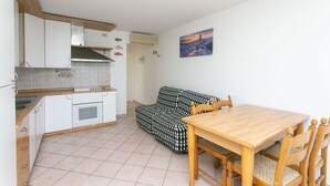 Una cuina petita amb armaris blancs, un frontissó de rajola, una taula de dinar de fusta i un sofà estampat.