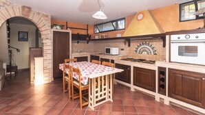 Una cocina con suelo de baldosas, una mesa con sillas, microondas, horno y una pared decorativa.