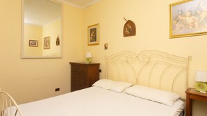 Un dormitorio con una cama, un tocador, una mesita de noche, un espejo y una pared con cuadros.