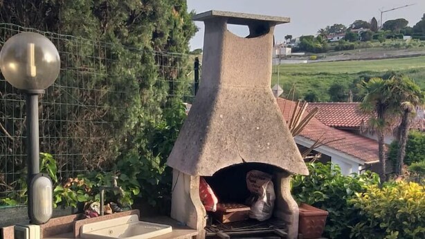 Una zona de cocina al aire libre con un horno de piedra, una mesa de metal y sillas.