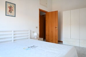 Une chambre à coucher comprenant un lit, une armoire en bois, une table de chevet et une porte donnant sur une autre pièce.