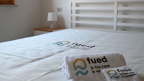 Un lit avec une couvre-lit blanche et une serviette ornée du logo « fued la tua casa in vacanza ».