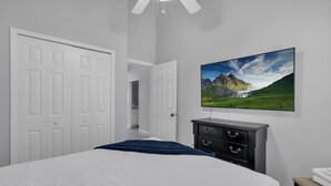 A bedroom with a bed, a dresser, a TV, and a door leading to another room.
