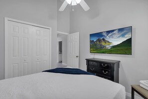 A bedroom with a bed, a dresser, a TV, and a door leading to another room.