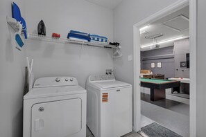 A laundry area with two washers and dryers, a shelf with folded towels, and a billiards table in the adjacent room.