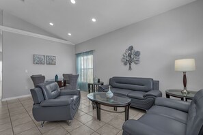 Uma sala de estar moderna com sofás cinza, uma mesa de centro de vidro e um objeto decorativo na parede.