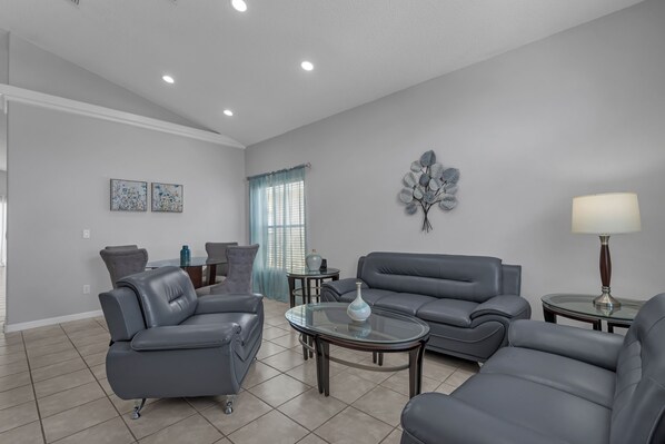 A modern living room with grey sofas, a glass coffee table, and a decorative wall piece.