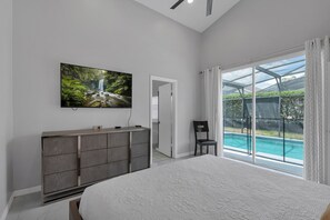 Quarto com uma cama grande, televisão na parede e vista para uma piscina através de portas de vidro.