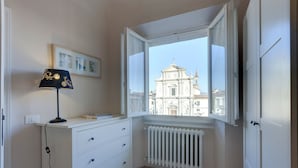 A room with a white dresser, a lamp, a radiator, and a window with a view of a historic building.