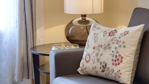 A room with a grey sofa, a round table with a lamp, and a floral pillow.