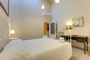 Ein ordentlich eingerichtetes Schlafzimmer mit Bett, Nachttisch, Schreibtisch, Stuhl und Klimaanlage.