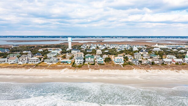 Un área residencial costera con casas a lo largo de la playa, un faro y vistas al océano.