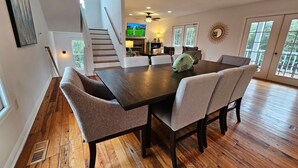 Un comedor con una mesa de madera oscura y cuatro sillas tapizadas. Una escultura decorativa de un pez se encuentra sobre la mesa. El piso es de madera y hay una escalera que conduce a otro nivel.