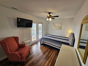 Une chambre à coucher avec un lit, une chaise, un téléviseur, un ventilateur de plafond et une fenêtre.