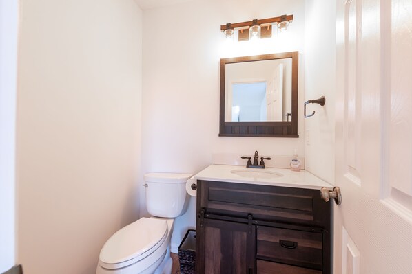 Une salle de bain avec des toilettes blanches, un lavabo surmonté d’un miroir et des meubles en bois foncé.