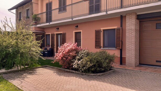 A two-story building with a brick facade, a balcony with wrought iron railings, and a small garden area with flowering bushes.