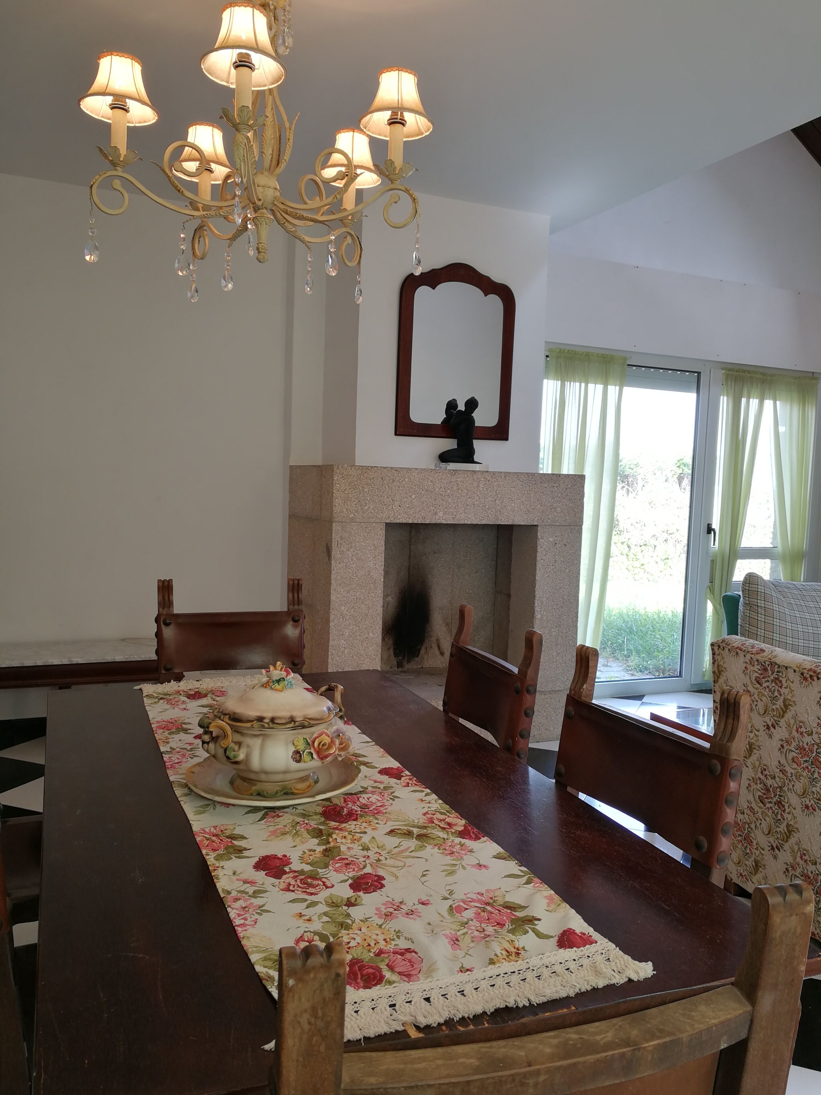 A dining room with a wooden table, floral tablecloth, and a chandelier.