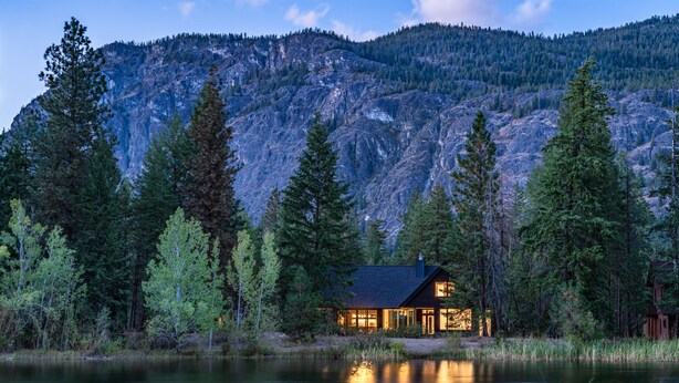 Une cabane au bord d’un lac, avec une chaîne de montagnes en arrière-plan.