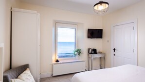 A bedroom with a bed, a window with a view, a bedside table with a lamp, and a television on the wall. - Manse On The Beach (Portaferry)