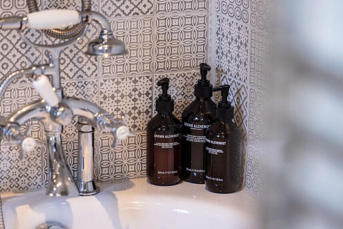 A bathroom with a sink, three bottles of 'Grown Alchemist' body care products, and a patterned tile backsplash.