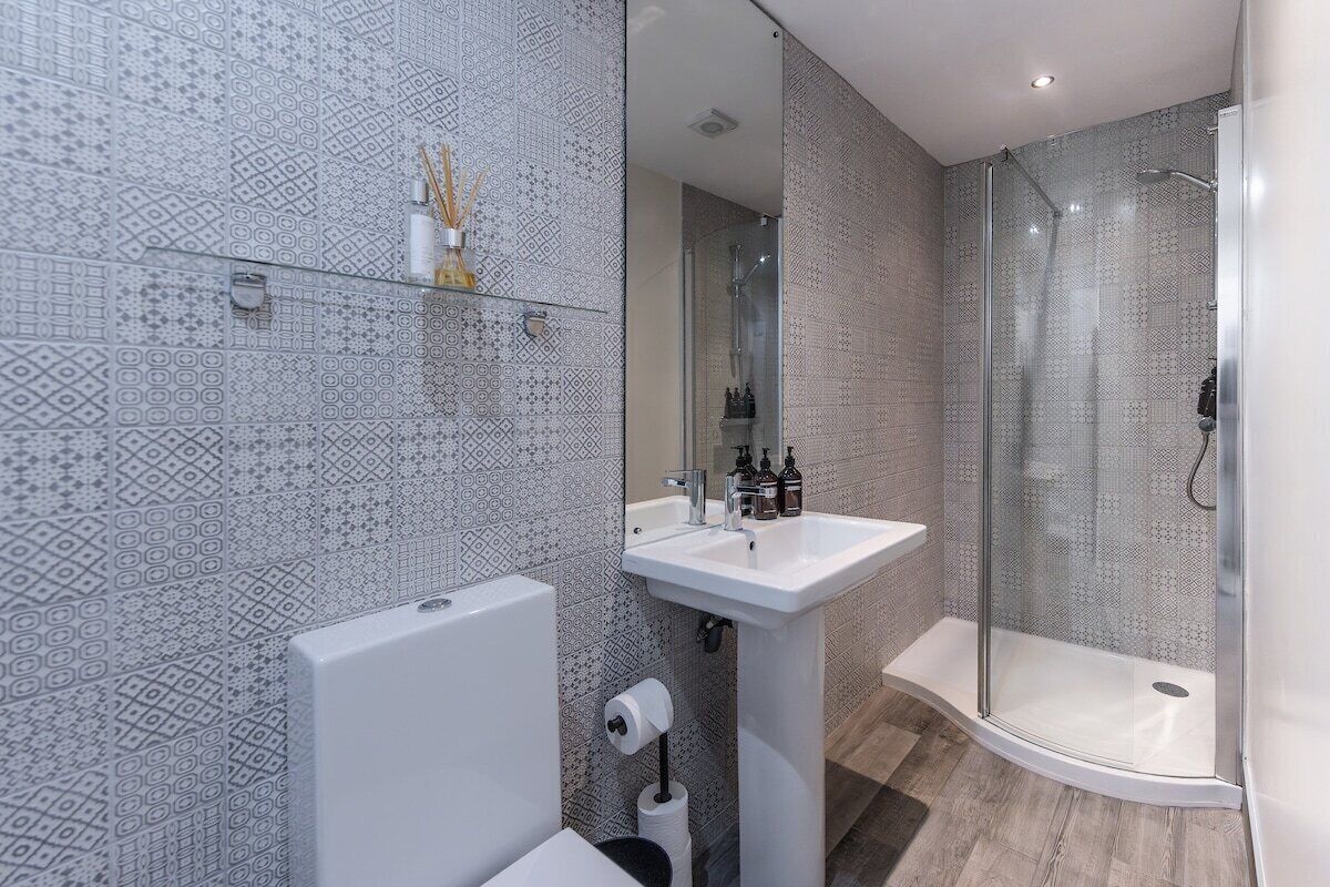 Un baño moderno con baldosas estampadas, cabina de ducha con mampara de vidrio, lavamanos blanco y un inodoro.