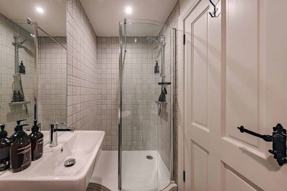 Un baño con ducha de vidrio, un lavamanos blanco con dispensadores de jabón y un espejo.