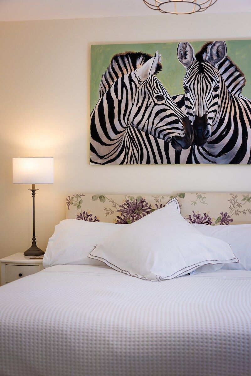A bedroom with a bed, a nightstand, a lamp, and a painting of zebras on the wall.