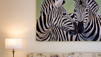 A bedroom with a bed, a nightstand, a lamp, and a painting of zebras on the wall.