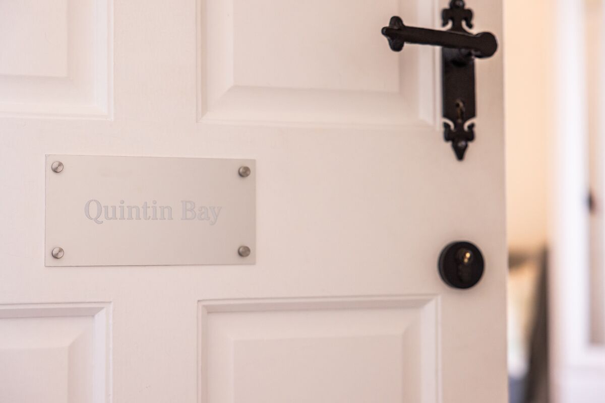 A white door with a nameplate reading "Quintin Bay" and a black door handle.