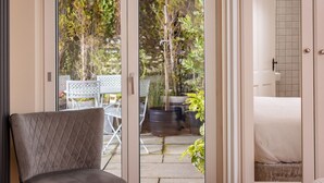A room with a sliding glass door leading to an outdoor patio area with a white table and chairs, potted plants, and a view of trees. - Manse On The Beach (Portaferry)
