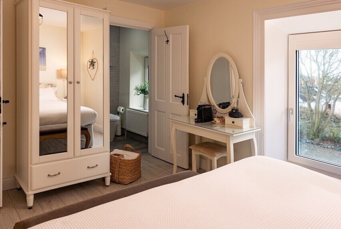 Un dormitorio con cama, armario de puertas de cristal, escritorio con espejo y vistas al exterior.