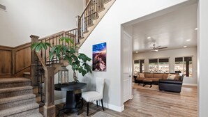 A spacious living area with a wooden staircase, a large plant, and a view of the outdoors through large windows. - Spacious, Private Hot Tub, 6 bedrooms 5 Ensuite Bathrooms. 7th night FREE!  (Orderville)