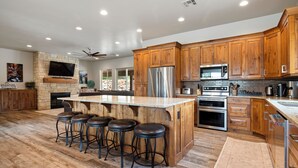 A modern kitchen with wooden cabinets, a central island with stools, stainless steel appliances, and a stone fireplace. - Spacious, Private Hot Tub, 6 bedrooms 5 Ensuite Bathrooms. 7th night FREE!  (Orderville)