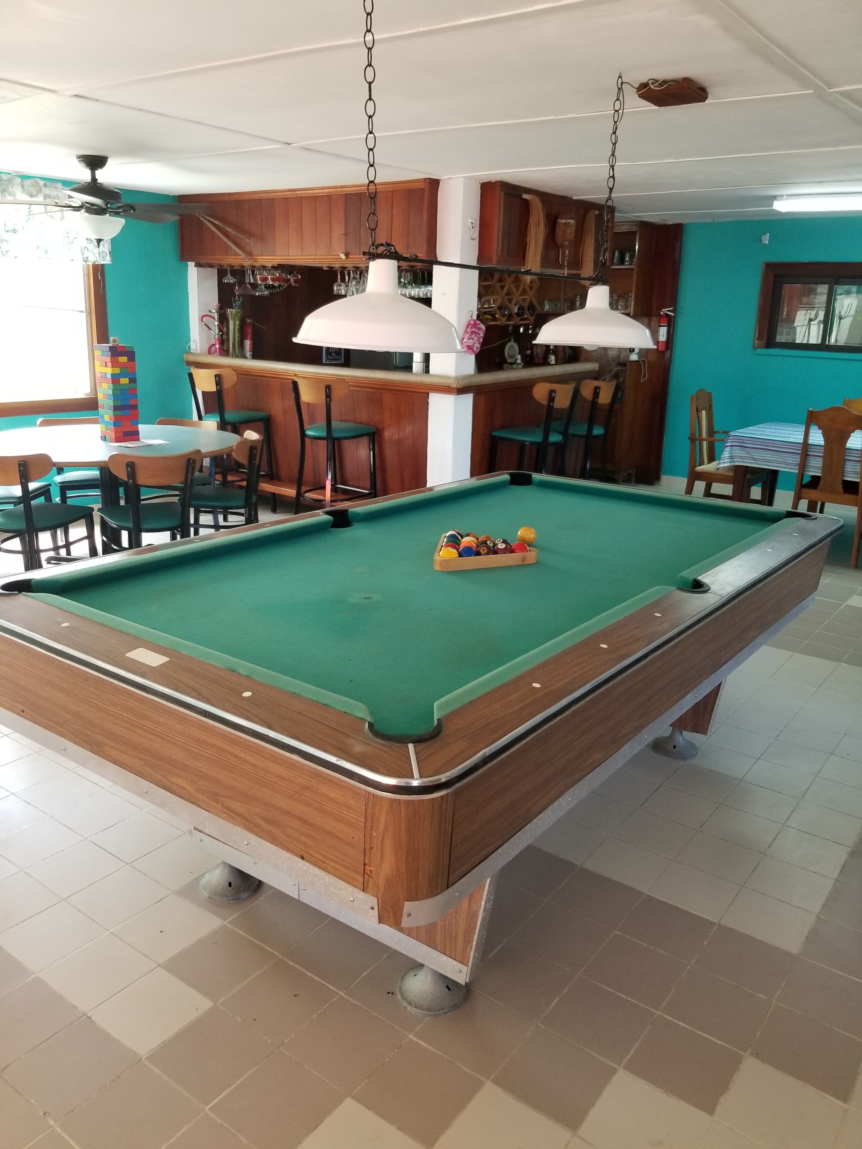 Una mesa de billar con bolas, una zona de bar con taburetes y un comedor con sillas.