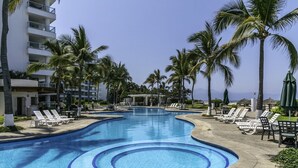 Una piscina con sillones de descanso y palmeras, rodeada por un edificio con balcones.