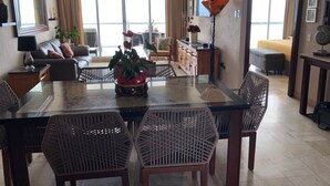 Un comedor con una mesa de vidrio, sillas de mimbre y vistas al exterior.