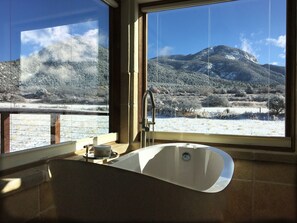 A bathroom with a large window offering a view of a snowy landscape and mountains.