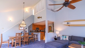 A modern living room with a grey sofa, wooden dining table, and chairs. A ceiling fan and pendant light are visible. - 3BR condo with A/C, pool & 10min walk to the beach! (Koloa)