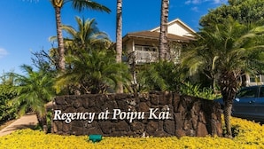 A stone sign with "Regency at Poipu Kai" written on it, surrounded by tropical vegetation and palm trees. - 3BR condo with A/C, pool & 10min walk to the beach! (Koloa)