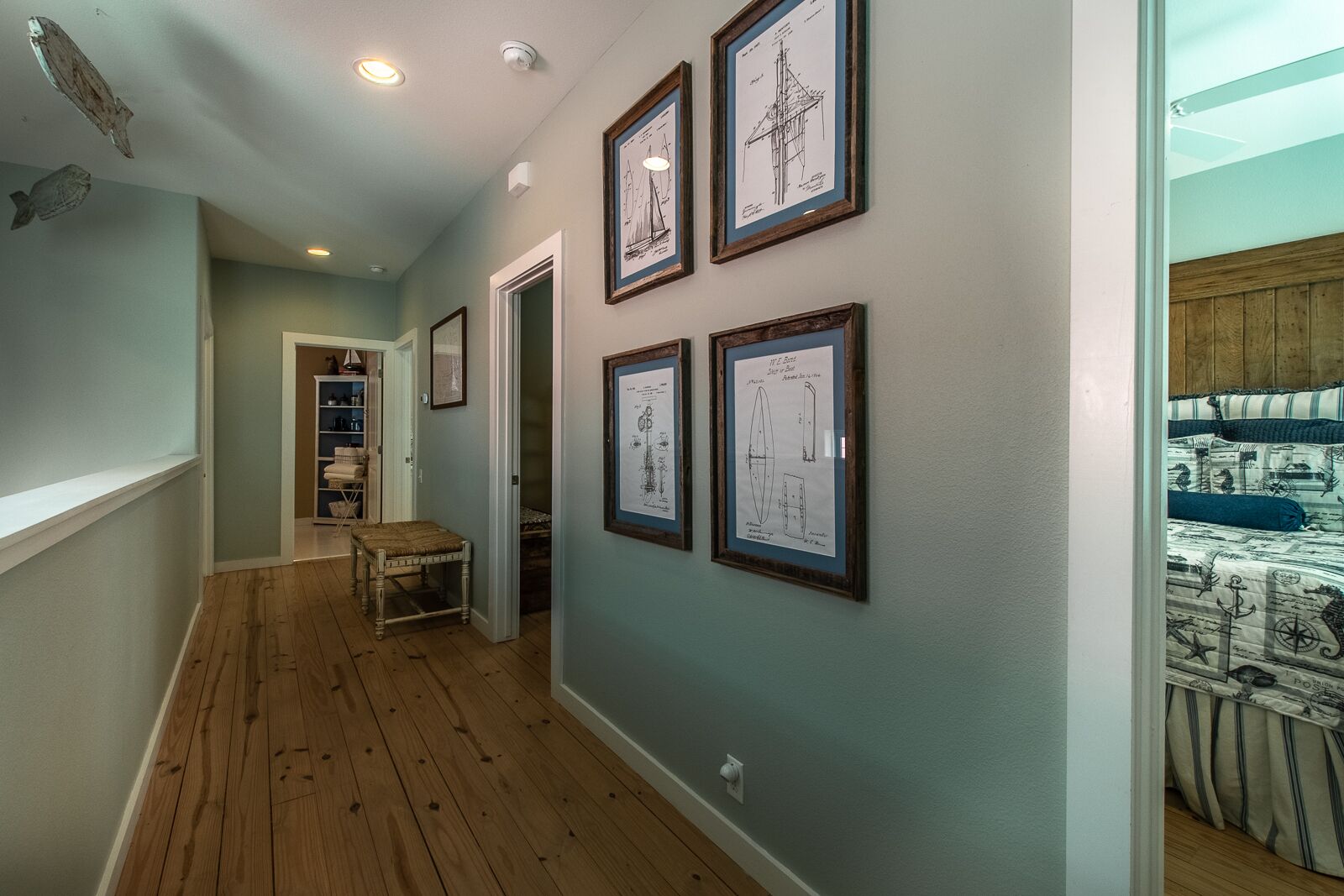 A hallway with wooden flooring, a bench, and framed architectural drawings on the wall.