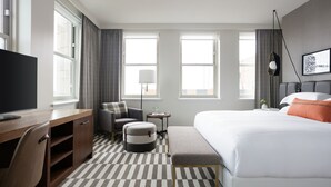 A hotel room with a bed, a desk, a chair, a small table, and a TV.