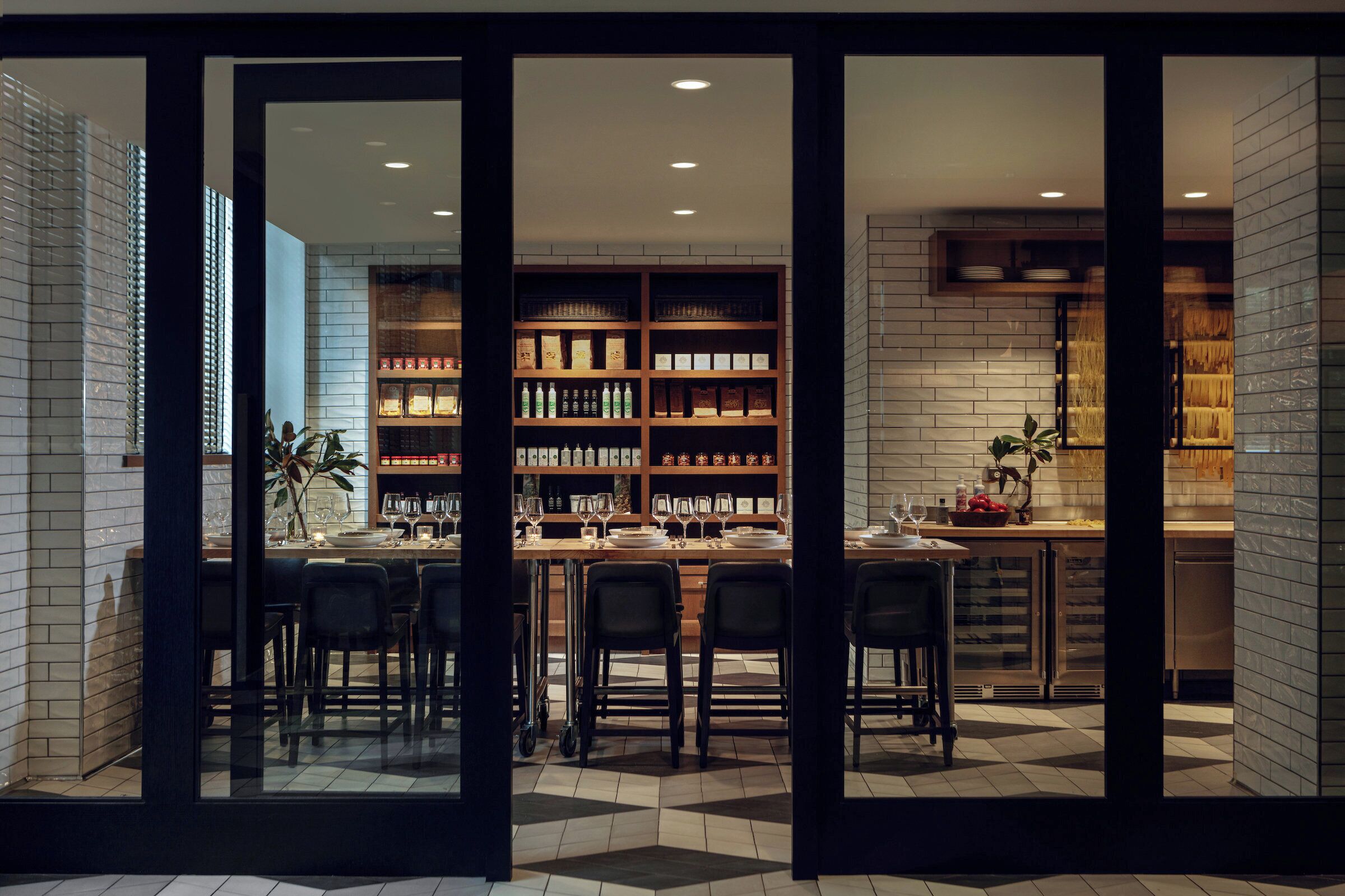 A modern interior with a bar area, seating, and a kitchen visible through glass doors.