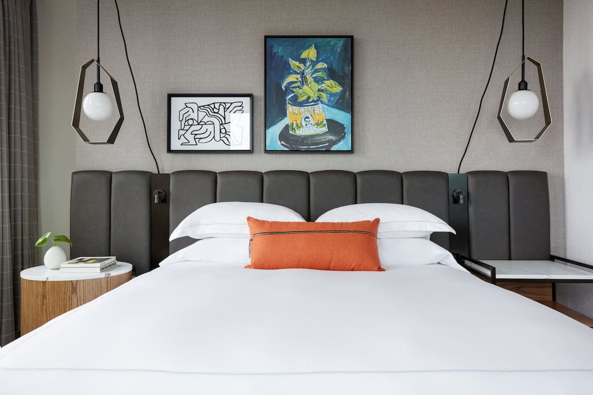 A modern hotel room with a large bed, two bedside tables, and artwork on the wall.
