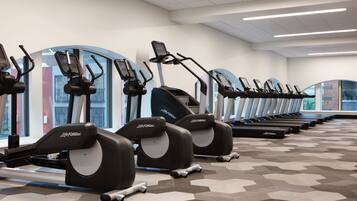 Une rangée de vélos d’appartement dans une salle de sport dotée de grandes fenêtres et d’un sol à motifs.
