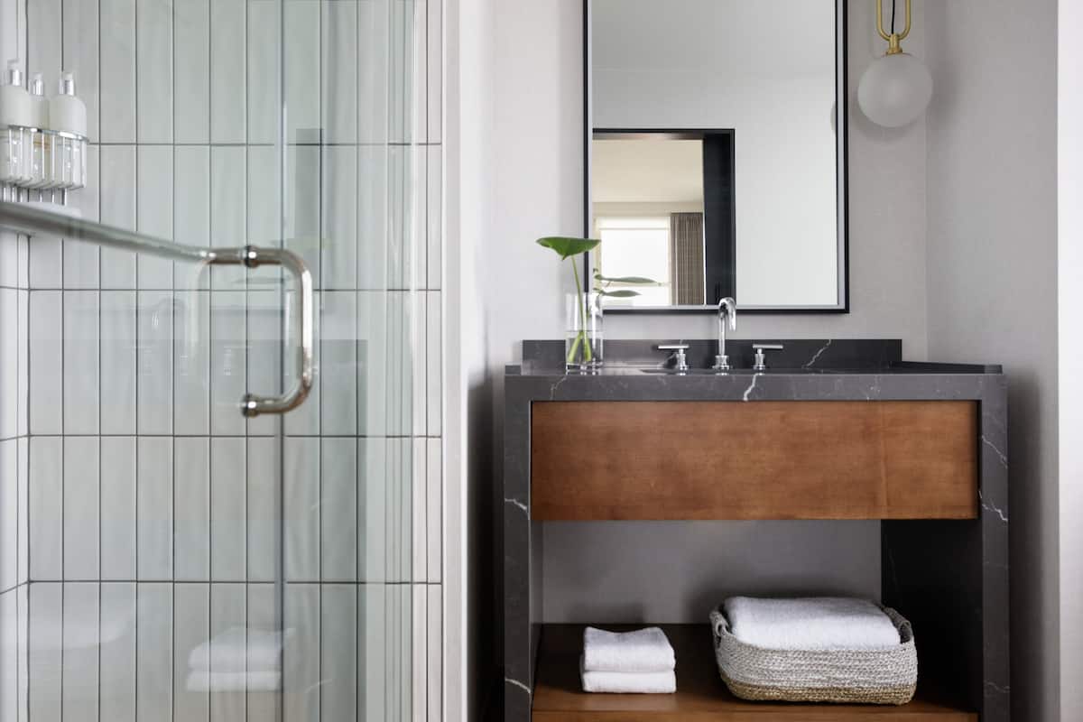 A modern bathroom with a glass shower enclosure, a wooden vanity with a marble countertop, and a large mirror above the sink.